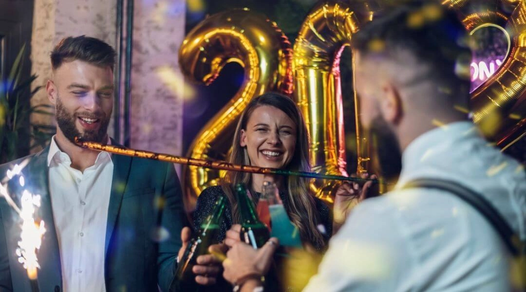 Grupa młodych osób świętująca sylwestra, z balonami 2026 w tle i zimnymi ogniami w rękach.