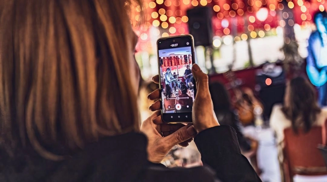 Kobieta nagrywająca telefonem koncert wśród kolorowych świateł i publiczności