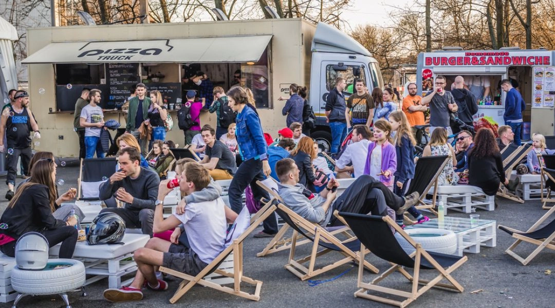 Food trucki i leżaki podczas festiwalu street food w Warszawie, ludzie siedzą i jedzą na świeżym powietrzu.