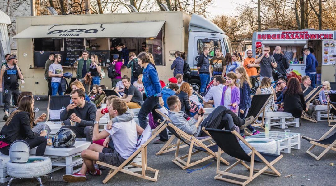 Food trucki i leżaki podczas festiwalu street food w Warszawie, ludzie siedzą i jedzą na świeżym powietrzu.