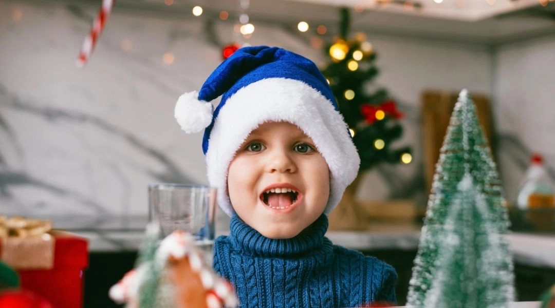 Uśmiechnięte dziecko w mikołajowej czapce podczas świątecznych warsztatów plastycznych.