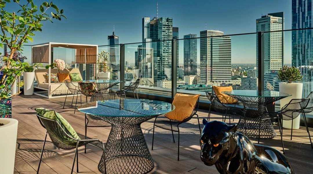 Stoliki i leżanki na dachu NYX Hotel Warsaw z panoramą wieżowców w centrum Warszawy.