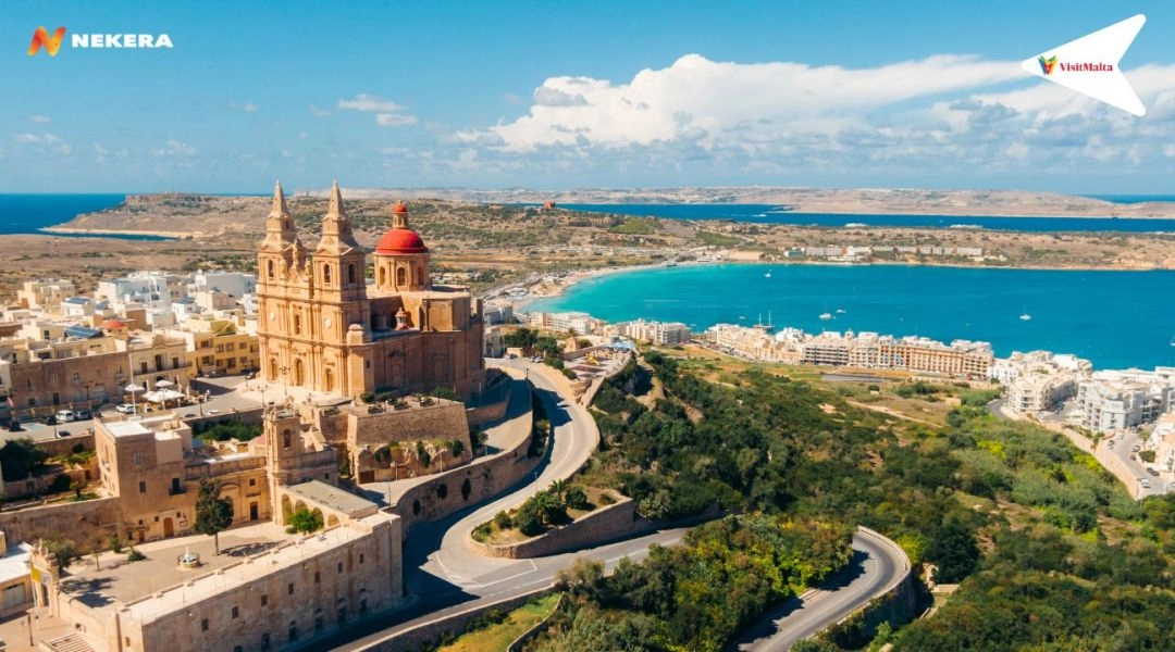 Północ Malty z widokiem na zatokę i zabudowę nadmorską, jasna plaża i błękitne morze.