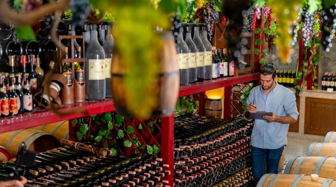 Piwnica z winem w Bordeaux, rzędy butelek, beczki i mężczyzna sprawdzający zapiski.