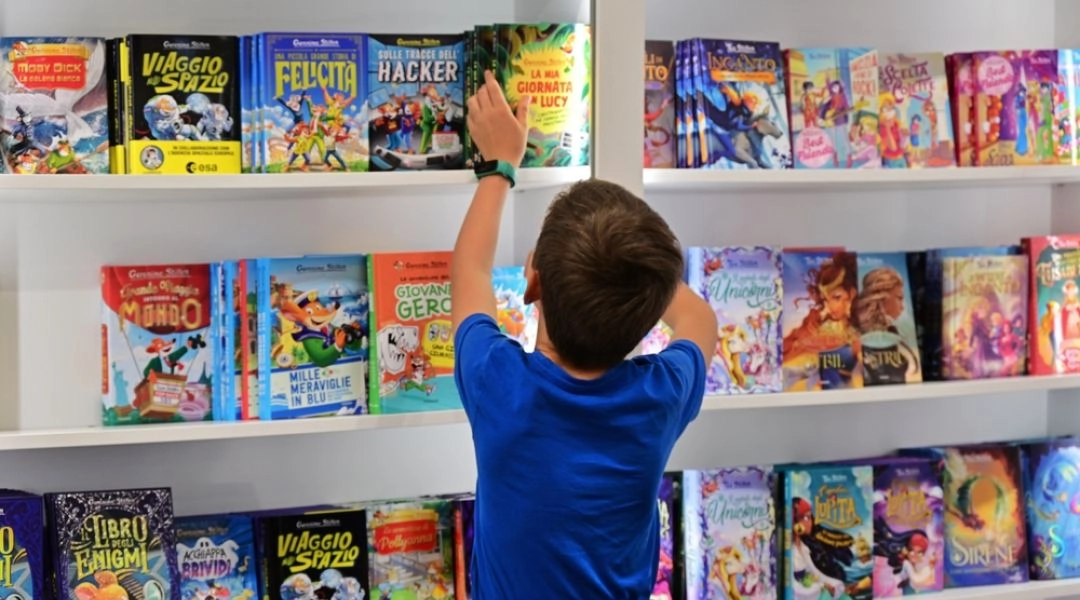 Dziecko wybierające książki z półki w bibliotece, spotkanie czytelnicze dla dzieci.