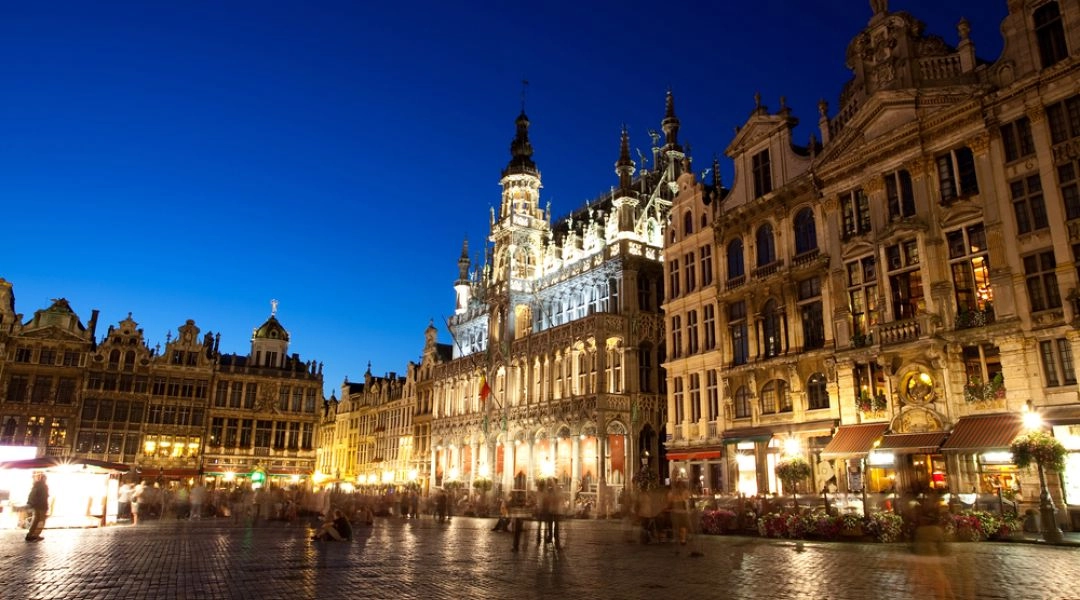 Grand-Place w Brukseli wieczorem, z podświetlonymi zabytkowymi kamienicami i ratuszem.
