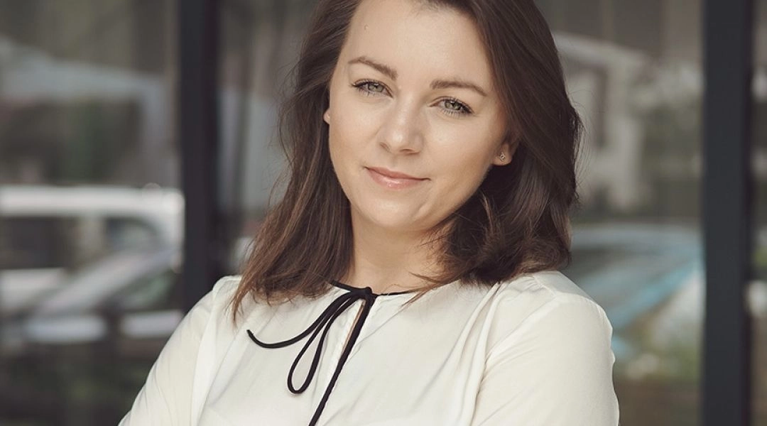 Małgorzata Gipsiak i jej portret w jasnej bluzce, stojącej ze skrzyżowanymi rękami przed przeszklonym budynkiem.