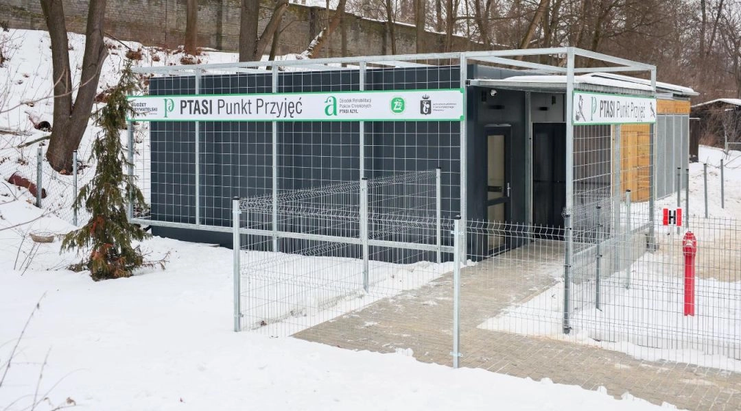 Budynek Ptasiego Punktu Przyjęć przy warszawskim zoo zimą, wejście ogrodzone metalowym płotem