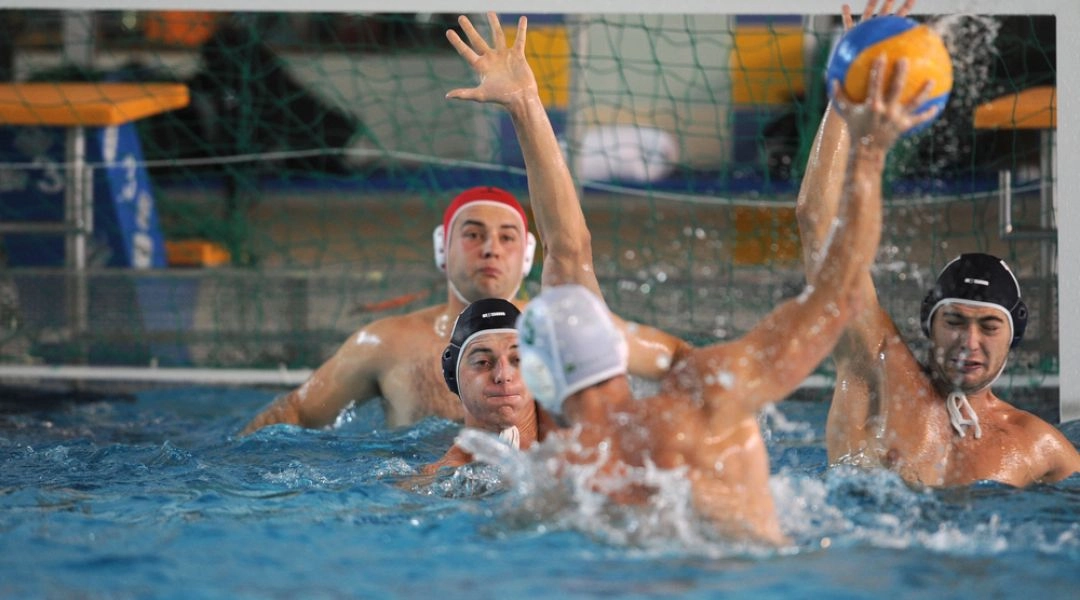 Zawodnicy waterpolo walczą o piłkę w basenie podczas meczu ligowego.