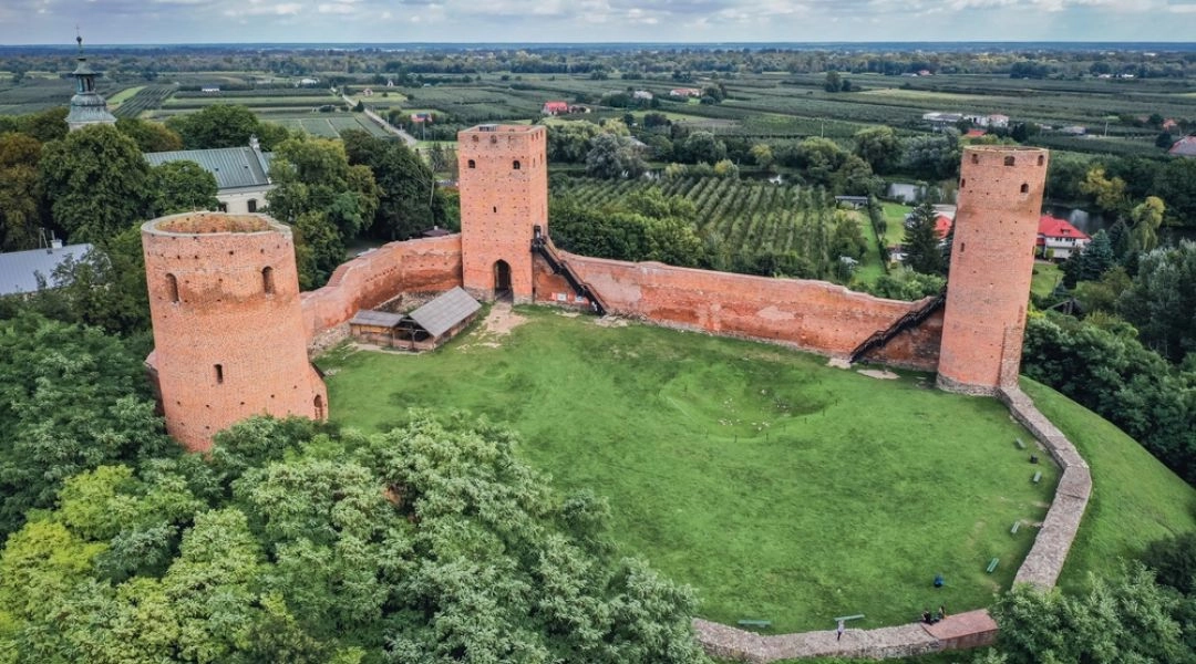 Zamek książąt mazowieckich w Czersku widziany z góry, z trzema ceglanymi wieżami, murami obronnymi i zielonym dziedzińcem.