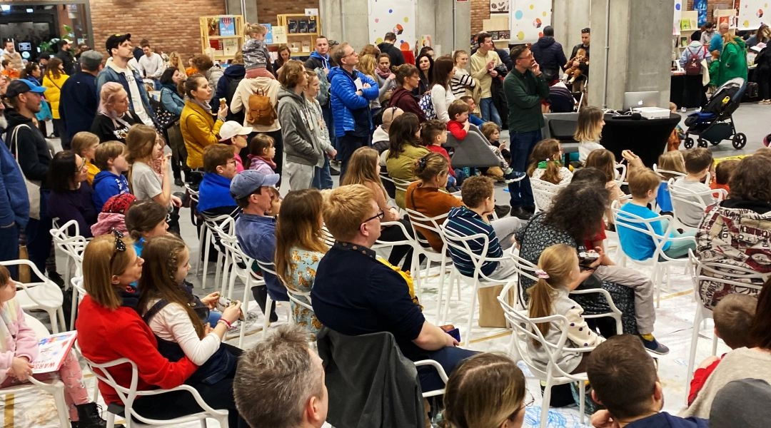 Tłum odwiedzających podczas targów książki dziecięcej Mały Koneser w Warszawie, stoiska wydawnictw i rodziny przeglądające książki.