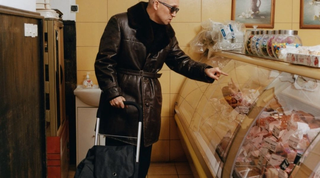 an Emil Młynarski w skórzanym płaszczu robi zakupy w tradycyjnym sklepie mięsnym.
