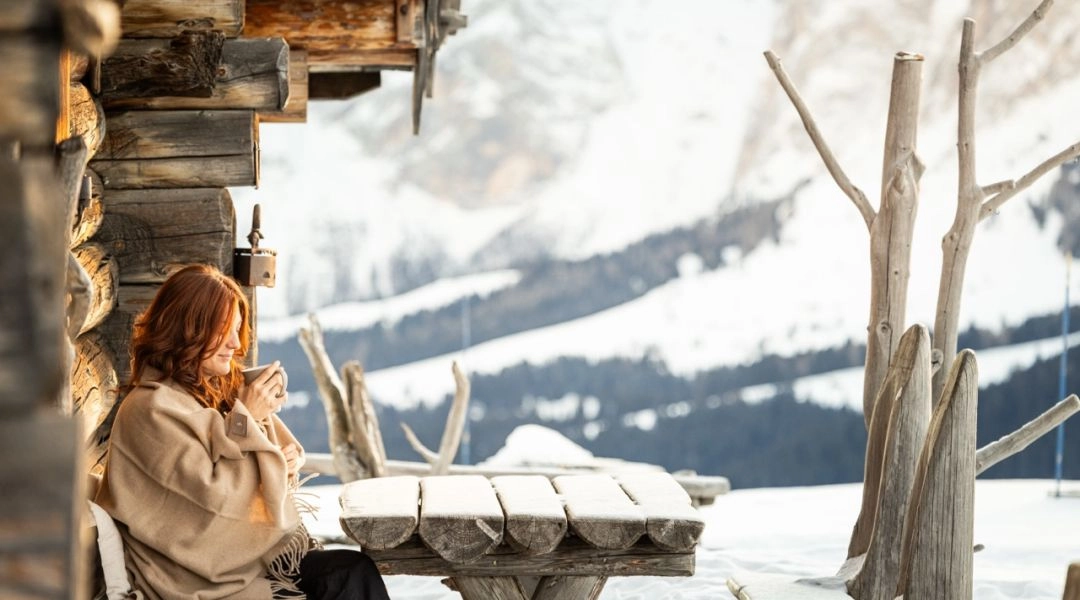 Zimowy wypoczynek w Południowym Tyrolu górskie schronisko i kobieta trzymająca w dłoniach kubek z gorącym napojem.