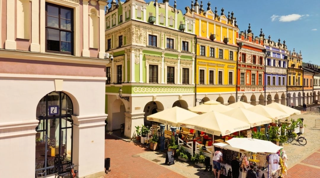 Kolorowe kamienice z arkadami i ogródki restauracyjne pod parasolami na Rynku Wielkim w Zamościu.