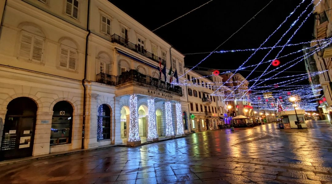 Ulica Korzo w Rijece nocą, z świątecznymi lampkami zawieszonymi nad deptakiem i oświetlonymi kamienicami.