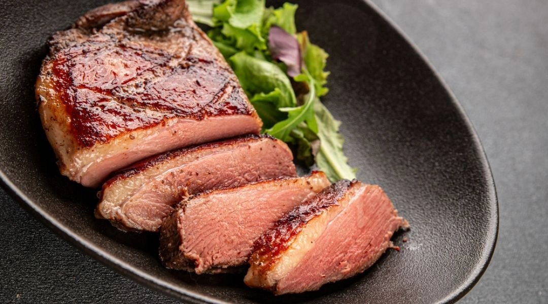 Pokrojona pierś z gęsi z chrupiącą skórką na czarnym talerzu z sałatką z liści.