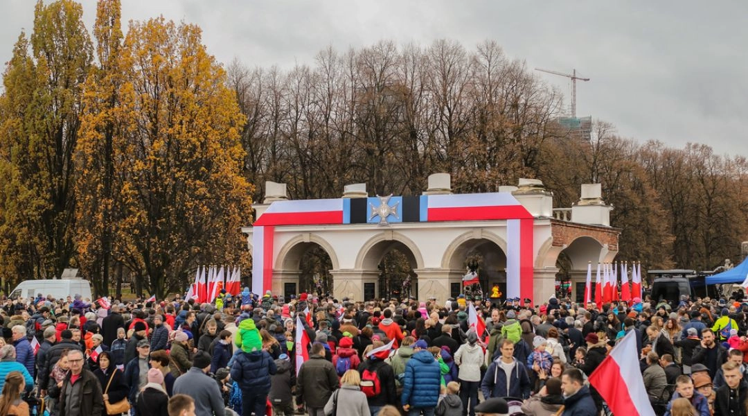 Warszawa 11 listopada, uroczystości pod Grobem Nieznanego Żołnierza, biało-czerwone flagi i jesienne drzewa w tle.