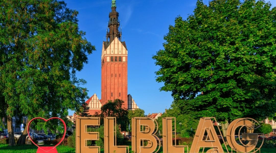 Napis I love Elbląg z katedrą św. Mikołaja w tle i zielenią miejskiego skweru.