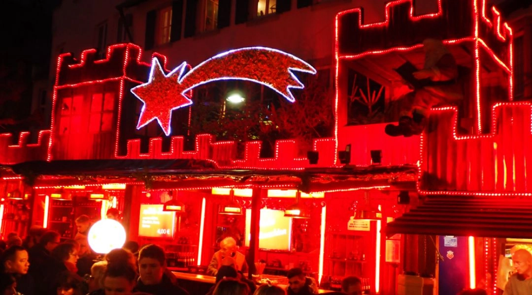 Stoisko jarmarku świątecznego w Rüdesheim nad Renem z intensywnym czerwonym oświetleniem i tłumem odwiedzających.