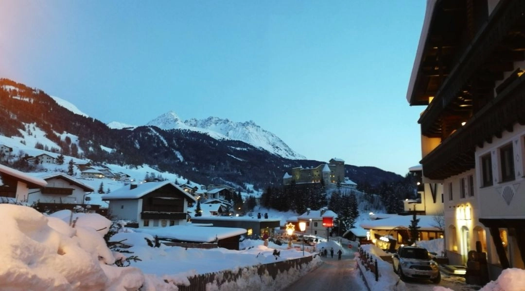 Wieczorna scena w Nauders zimą, taras hotelowy i oświetlona ulica w alpejskim miasteczku.