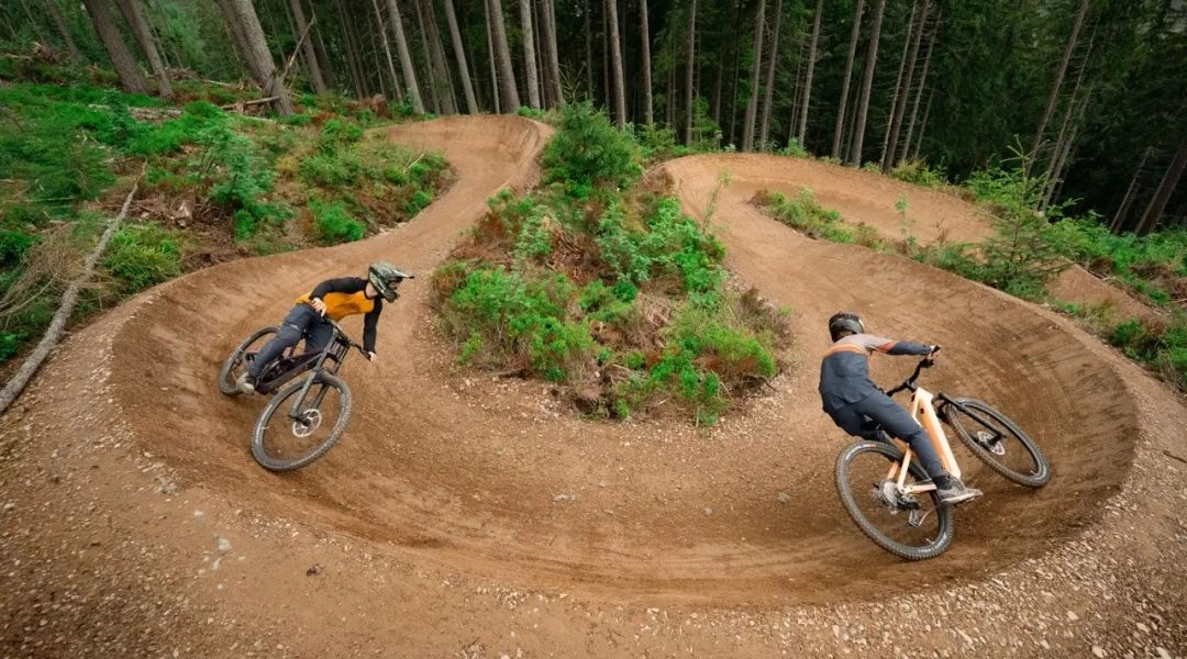 Dwóch rowerzystów pokonuje wyprofilowane zakręty na leśnej trasie w Riders Park Donovaly.