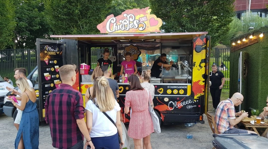 Ludzie stojący przy food trucku podczas festiwalu jedzenia na świeżym powietrzu w Warszawie.