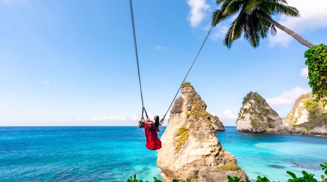 Kobieta na huśtawce zawieszonej nad turkusową wodą przy klifach Diamond Beach, Nusa Penida, Indonezja.