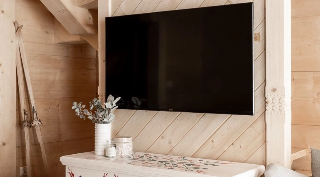 Drewniane wnętrze z telewizorem i ozdobną skrzynią z motywem ludowym.