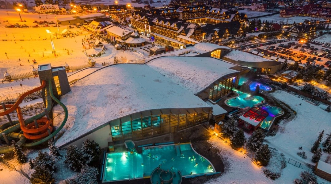 Nocny widok na kompleks Terma Bania w Białce Tatrzańskiej, ośnieżone dachy i parujące baseny.