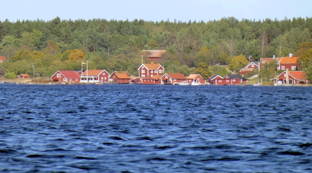 Nadmorska osada z czerwonymi drewnianymi domami nad wodami szwedzkiego archipelagu.