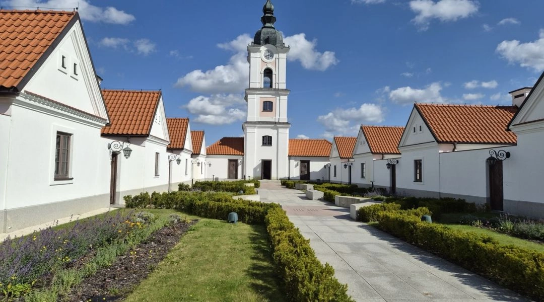 Dziedziniec Pokamedulskiego Zespołu Klasztornego w Wigrach z białymi eremami, czerwonymi dachami i wieżą zegarową.