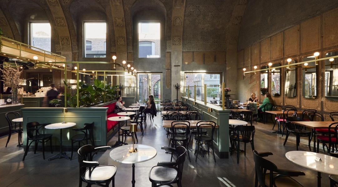 Przestronne wnętrze Petit Paris w Poznaniu z wysokimi oknami, stolikami i zachowanymi elementami zabytkowej architektury.