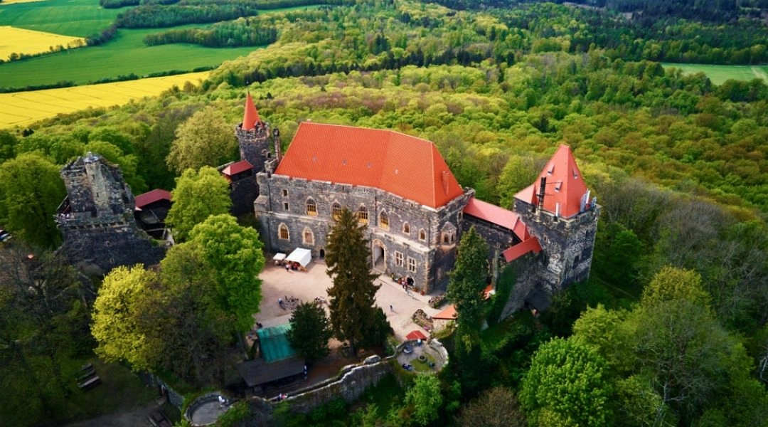 Zamek Grodziec widziany z lotu ptaka, położony na zalesionym wzgórzu i otoczony polami.