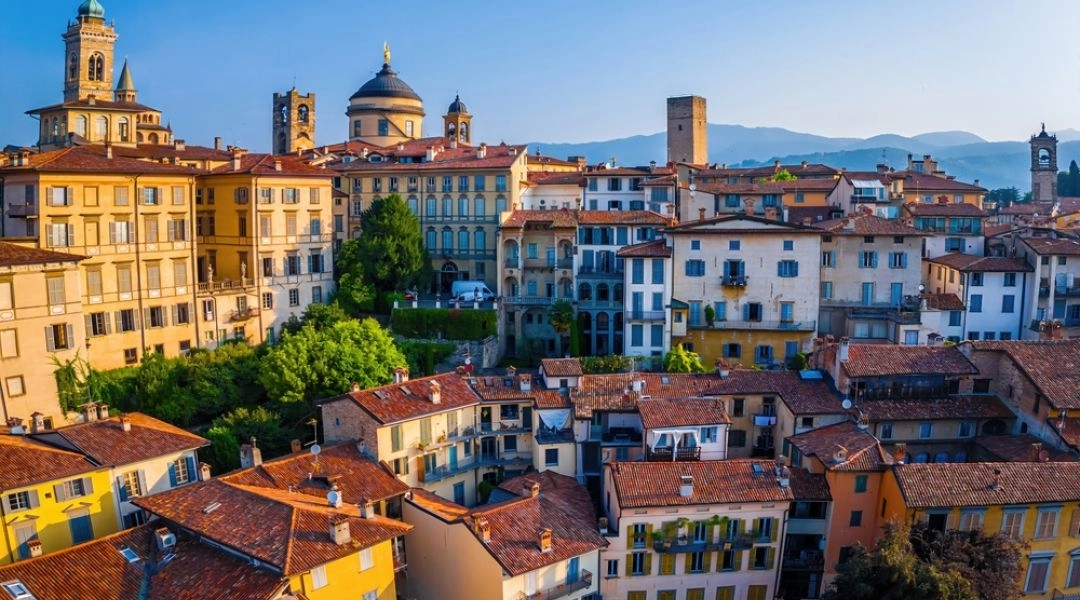 Panorama historycznej części Bergamo z kolorowymi kamienicami, wieżami i dachami na tle gór.