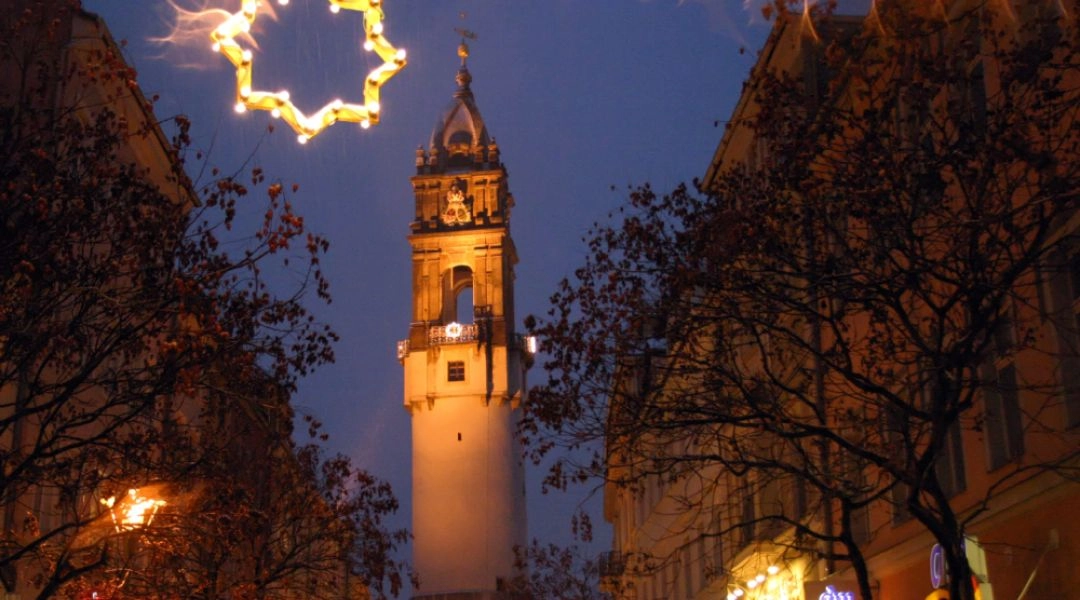 Podświetlona wieża miejska w Budziszynie otoczona świątecznymi ozdobami i stoiskami jarmarku.