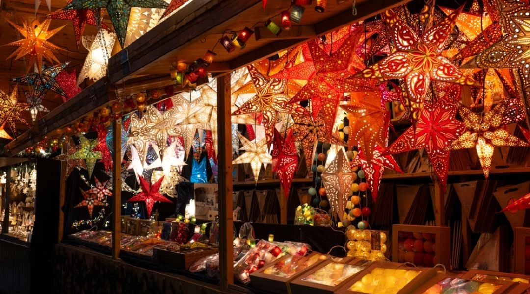 Drewniany domek gastronomiczny na jarmarku świątecznym w Warszawie, sprzedawcy i odwiedzający przy stoisku z vin chaud.