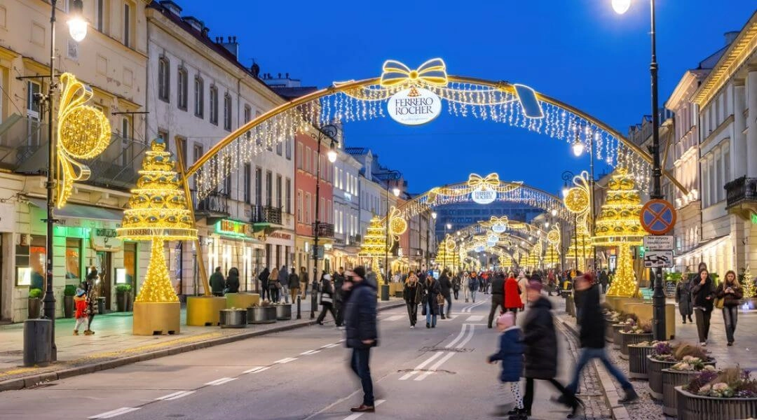 Świąteczne iluminacje na Krakowskim Przedmieściu w Warszawie nocą: świetlne bramy, choinki i spacerujący ludzie zimą.