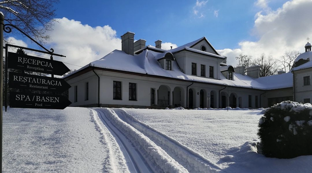 Zimowy Dwór Kombornia i historyczny budynek otoczony śniegiem, widok na główne wejście i drogę prowadzącą przez zaśnieżony teren.