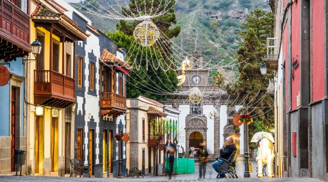 Ulica na Teneryfie ozdobiona świątecznymi lampkami, z tradycyjnymi kanaryjskimi domami i kościołem w tle.