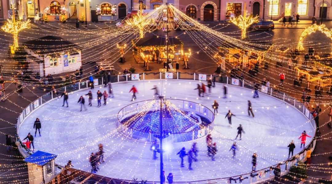Okrągłe lodowisko na Rynku Starego Miasta w Warszawie nocą, z osobami jeżdżącymi na łyżwach, iluminacjami świątecznymi i zabytkowymi kamienicami w tle.