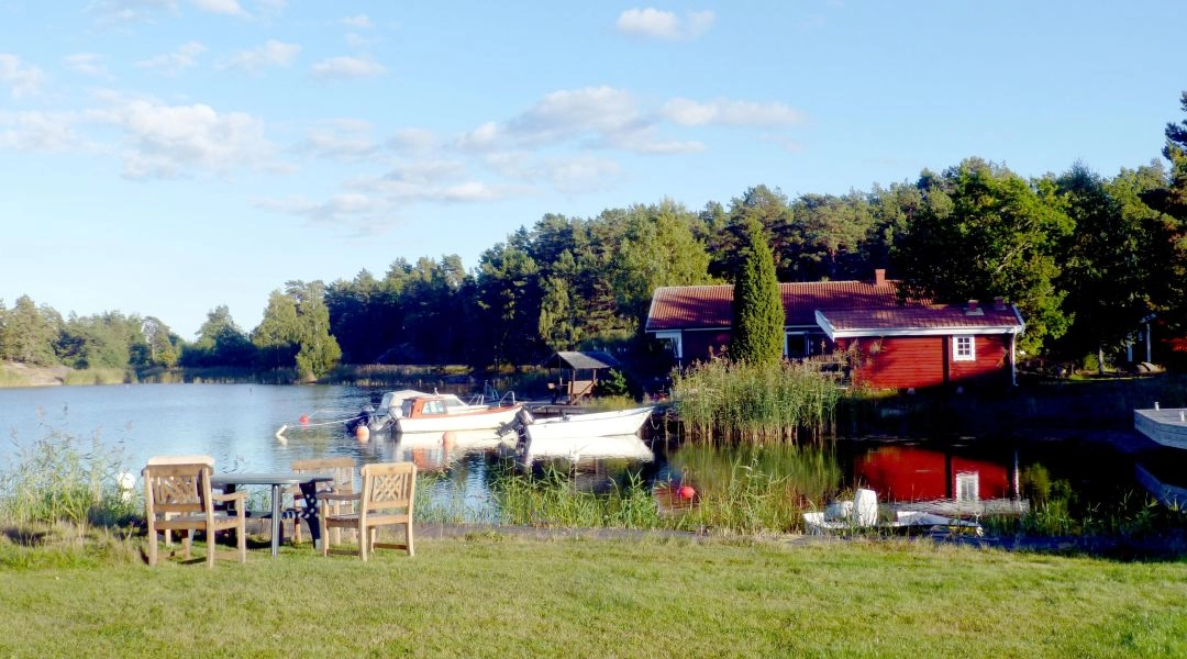 Czerwony dom i zacumowane łodzie nad spokojną zatoką w szwedzkich szkierach.
