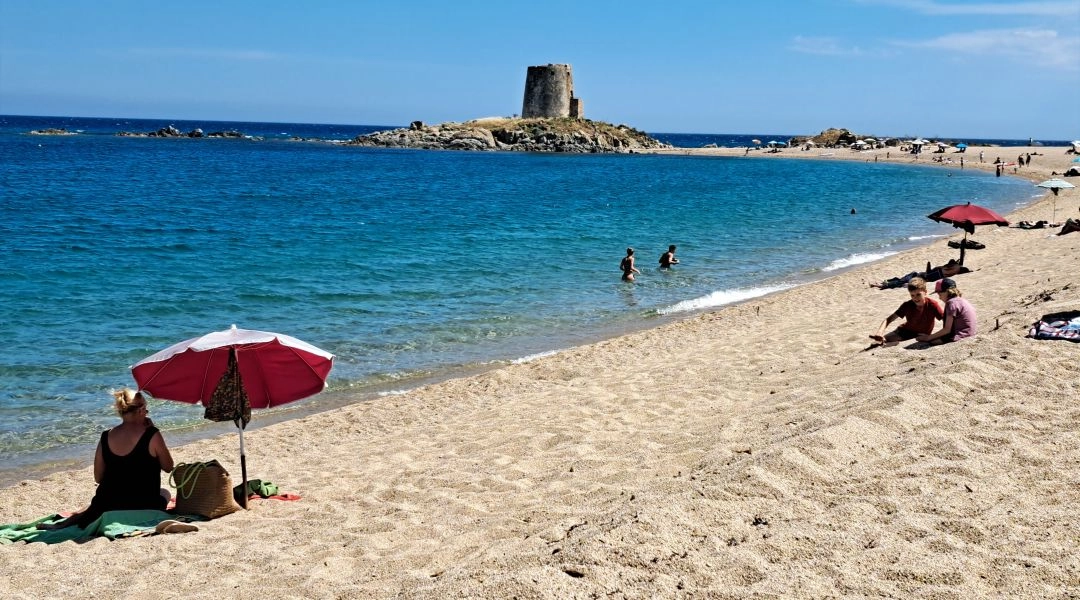 Piaszczysta plaża z turkusową wodą i zabytkową wieżą Torre della Pelosa na północy Sardynii.