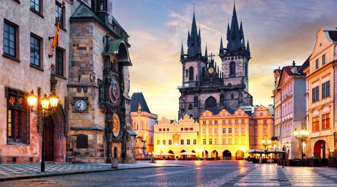 Rynek Staromiejski w Pradze o zmierzchu, z zegarem astronomicznym po lewej i wieżami kościoła Marii Panny przed Tynem w tle.