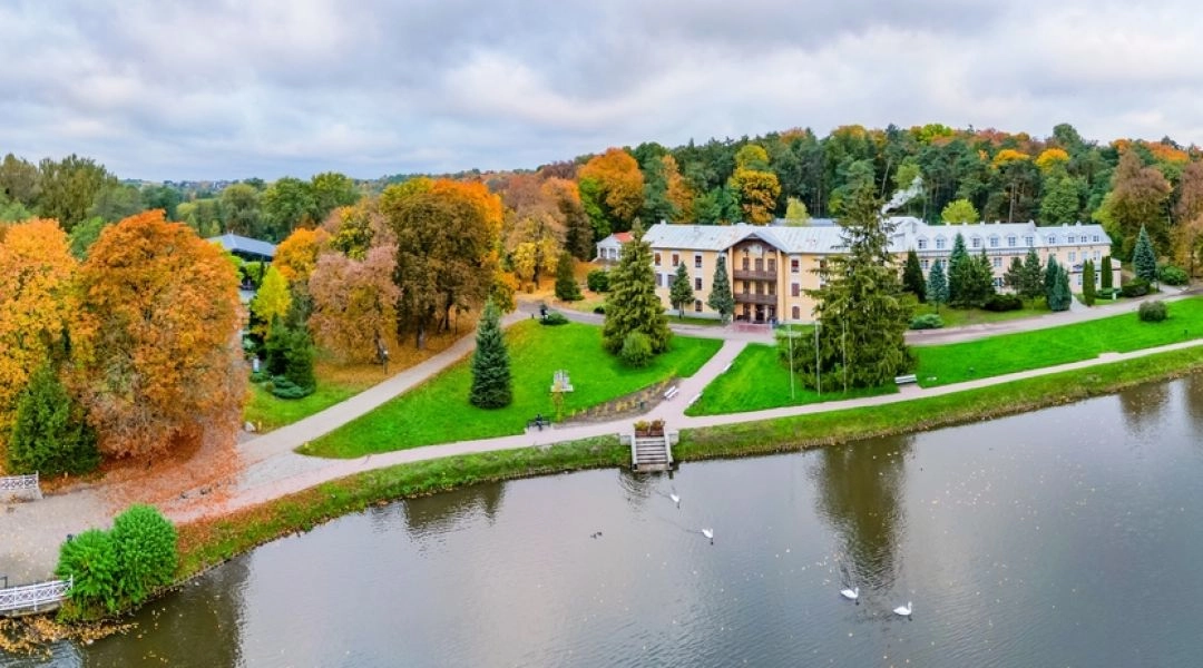 Jesienny Park Zdrojowy w Nałęczowie z aleją spacerową, stawem, drzewami i zabudową uzdrowiskową.