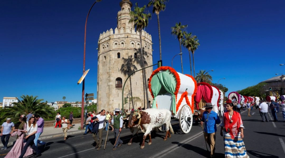 Uczestnicy pielgrzymki El Rocío przy Złotej Wieży w Sewilli, z ozdobnymi wozami i tradycyjnymi strojami.