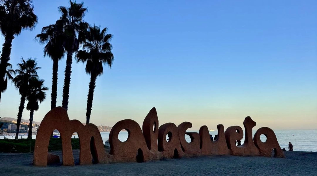 Napis Malagueta na piaszczystej plaży w Maladze, palmy i Morze Śródziemne