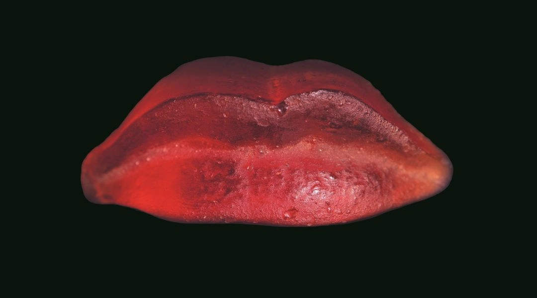 Czerwony odlew ust Aliny Szapocznikow pokazany na ciemnym tle.