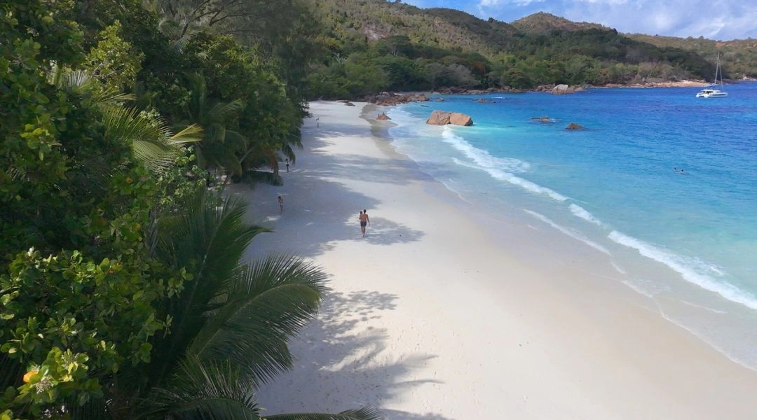 Pusta plaża Anse Lazio na wyspie Praslin z białym piaskiem, turkusowym oceanem, palmami i zielonym wzgórzem w tle.