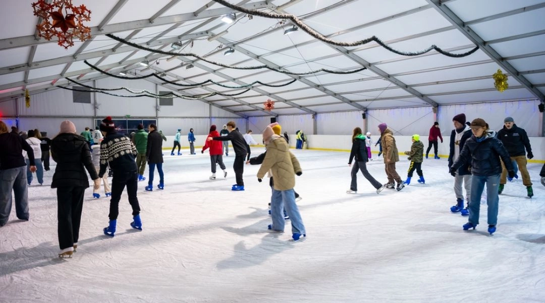 Tłum łyżwiarzy na zadaszonym lodowisku OSiR Targówek, dekoracje świąteczne wiszą pod sufitem hali.