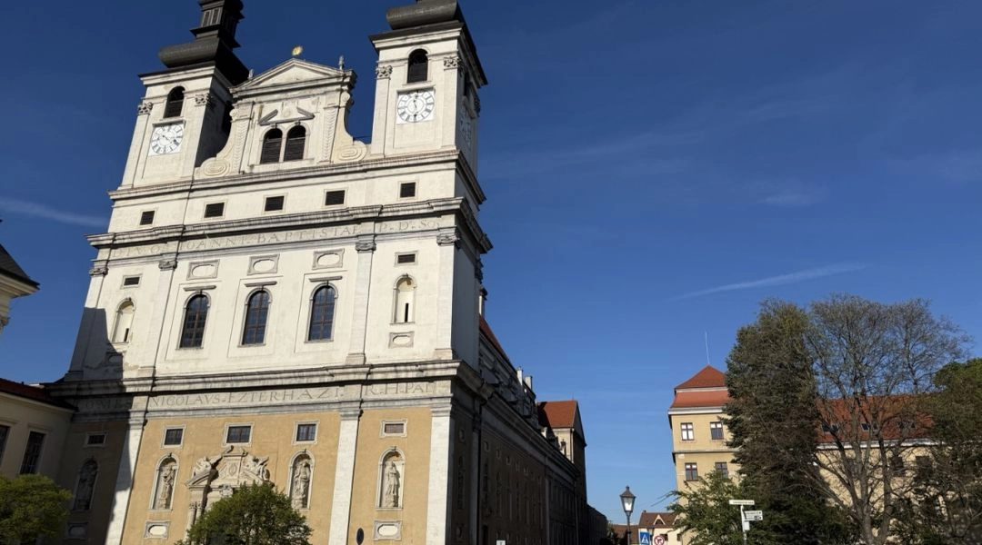 Fasada katedry św. Jana Chrzciciela w Trnawie z dwiema wieżami i jasną elewacją na tle błękitnego nieba.